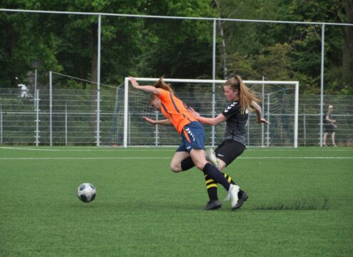 女子サッカーの試合中、選手同士の下肢が接触し、バランスを崩して転倒しそうになっている場面。下腿部打撲が起こる受傷機転のイメージ。